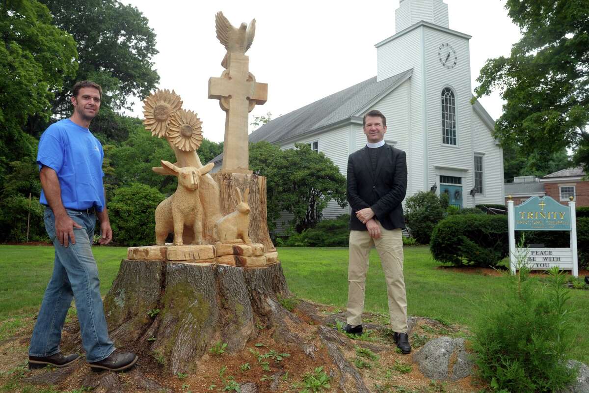 Sculptor Jared Welcomes, left, and Rev. Alan Murchie stand next to the new sculpture carved out of the truck of an old Maple tree in front Trinity Episcopal Church, in the Nichols neighborhood of Trumbull on Friday.