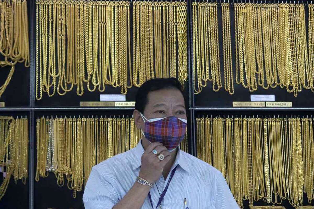 FILE - In this April 16, 2020, file photo, a Thai shopkeeper adjusts his face mask at a gold shop in Bangkok, Thailand. The price of gold surged more than $30 on Monday, July 27, 2020 to over $1,926 per ounce as investors step up buying of the precious metal often sought in times of uncertainty. Gold was trading at $1,926.20 by early afternoon in Asia, up 1.5%, after surging over the weekend.