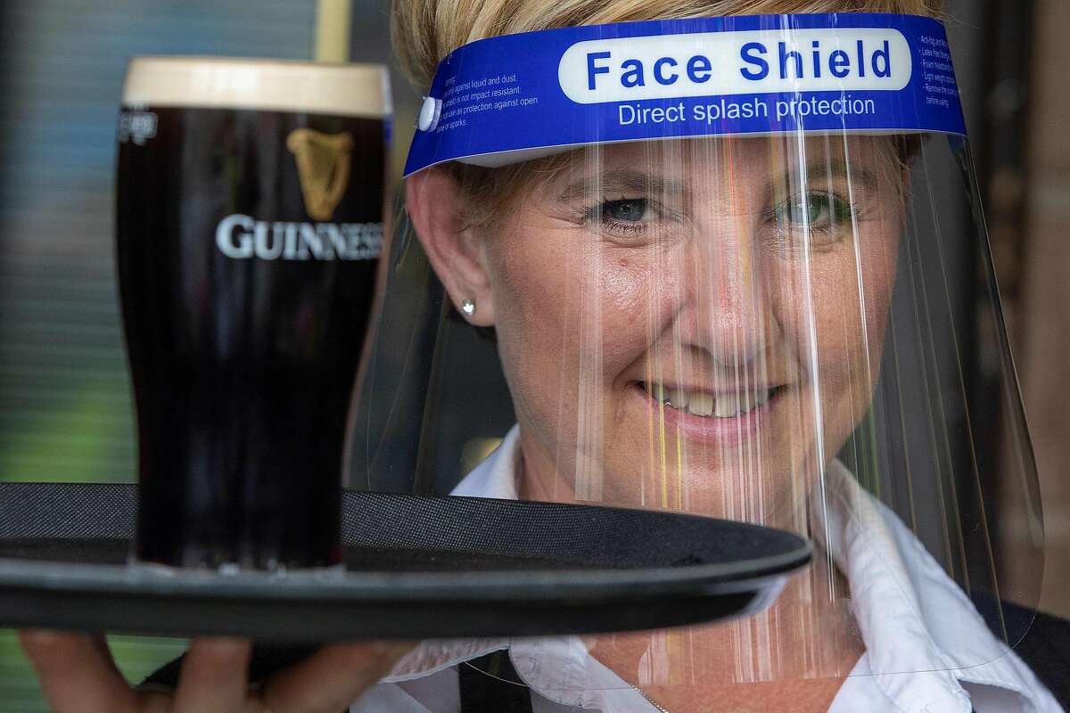 FILE — An employee of Murray's Bar in Dublin, Ireland, wears a face shield as a precautionary measure against spreading COVID-19.