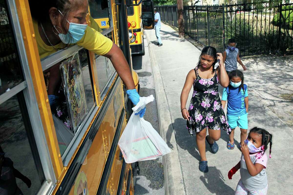Oralia Santos hands out bags of of reading material as the SAISD Foundation gives away books from a school bus parked at the Rosemont Apartments on Rigsby to local residents on July 28, 2020.