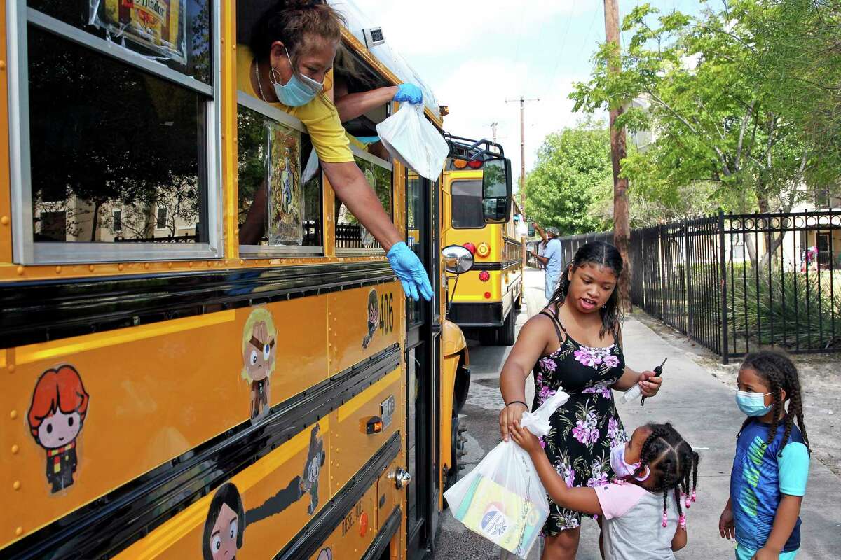 Oralia Santos hands out bags of reading material as the SAISD Foundation gives away books from a school bus parked at the Rosemont Apartments on Rigsby to local residents on July 28, 2020.