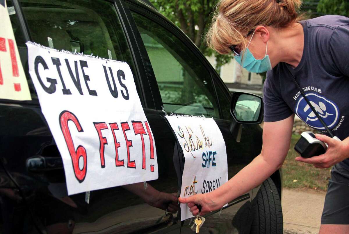 Janet Jacobs, a teacher at Wolfpit Elementary School, puts posters on her vehicle before the start of a "School Safety First" teacher caravan at Brien McMahon High School in Norwalk, Conn., on Thursday July 29, 2020. This was one of many held all across the state today. The purpose of the coordinated day of action is to amplify demands for safety and health precautions and full, equitable funding when school buildings reopen this fall.