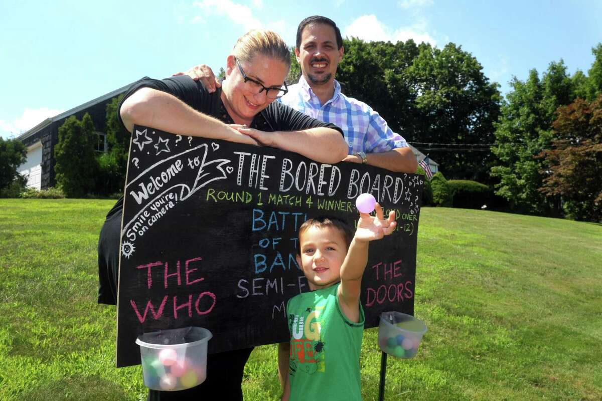 Jaimee and Brian Solomon pose next to their “Bored Board” with their son, Peter, in front of their Trumbull, Conn. home July 29, 2020.