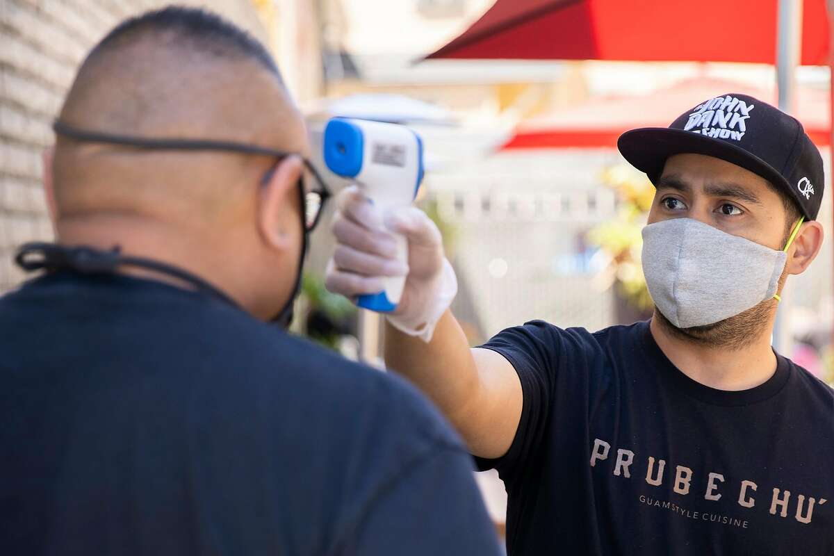 From right: Prubechu co-owner Shawn Camacho checks the temperature of customer Mateo Montez before letting him into the outdoor seating area on Thursday, July 30, 2020, in San Francisco, Calif. Prubechu has strict policies in place when it comes to health and safety, amid the coronavirus pandemic. Customers must fill out a health declaration, contact tracing form and have their temperature checked, among other rules, before entering the outdoor seating area.