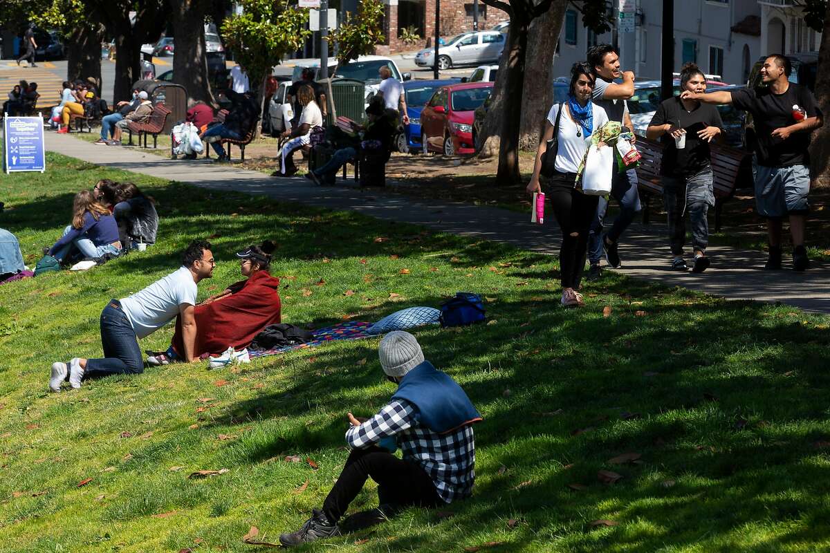 A group of people walk along the sidewalk without their masks on as they find a spot at Dolores Park on Tuesday, July 28, 2020, in San Francisco, Calif.