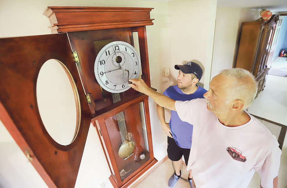 Kevin T. Goss, right, inserts the winding handle into the E.L. Barnard clock he is passing down to his son, Kevin W. Goss, left, at his rural Brighton home. This will be the third generation to treasure the 116-year-old clock.