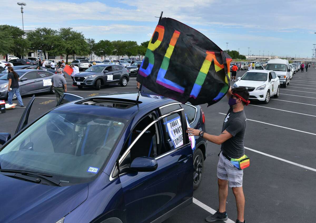 Jemm Corona-Morris adjusts a flag on his vehicle prior to a Black Lives Matter National Day of Action car caravan and food drive that began at the ATT Center and traversed along Commerce Street to Monterey Park on the west side.