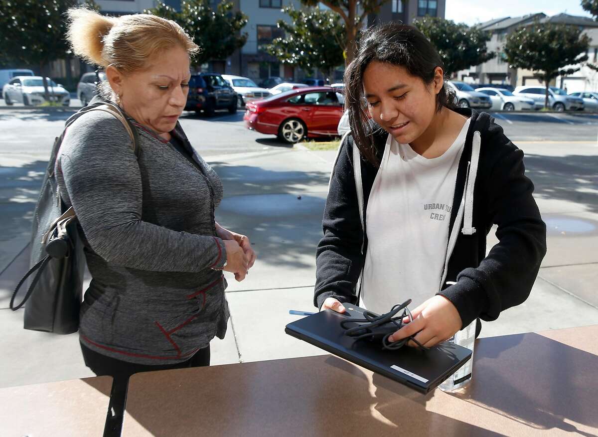Martha Sanchez (right), a sixth grader at Burbank Elementary School, picks up a Chromebook with her mother Maria Andrade in Hayward, Calif. on Wednesday, March 25, 2020. About 150 of the laptops were made available for students to participate in their school studies while sheltering at home during the coronavirus pandemic.