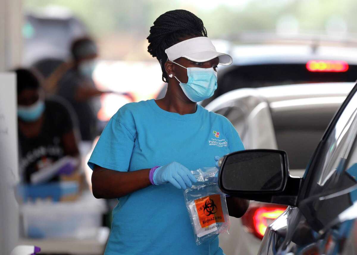 A woman brings testing supplies to a patient for a self-administered coronavirus test at Pridgeon Stadium, one of Harris County Public Health's eight coronavirus testing sites, Friday, July 31, 2020, in Cypress.