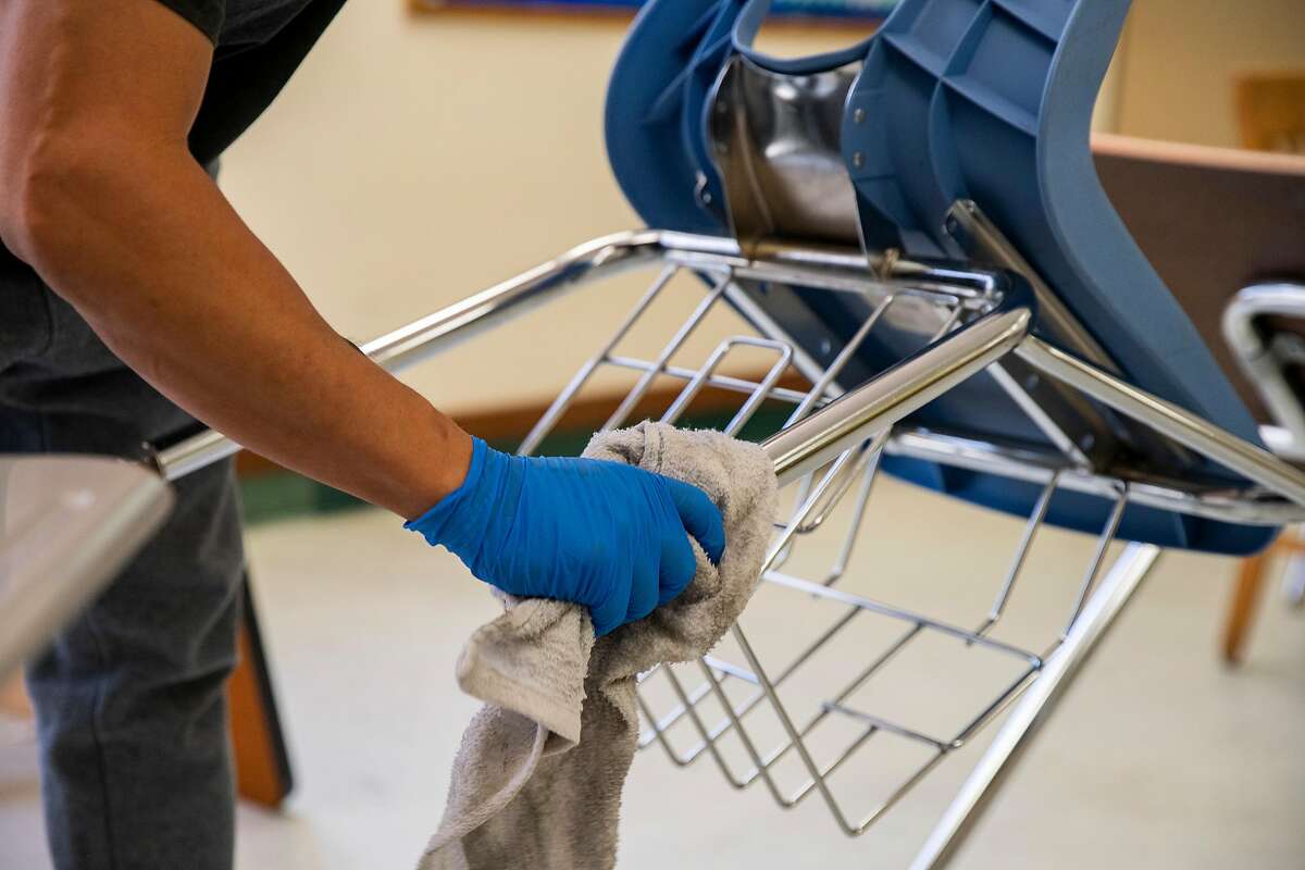 Custodian Orlando Lavarias cleans and sanitizes a chair inside a classroom that will be set up for physical distancing at Westlake Middle School on Friday, July 10, 2020, in Oakland, Calif. Schools are planning on how to reopen in the fall to ensure the safety and wellbeing of students and staff, amid the coronavirus pandemic. The middle school also holds the MetWest High School Ericka Huggins Campus.