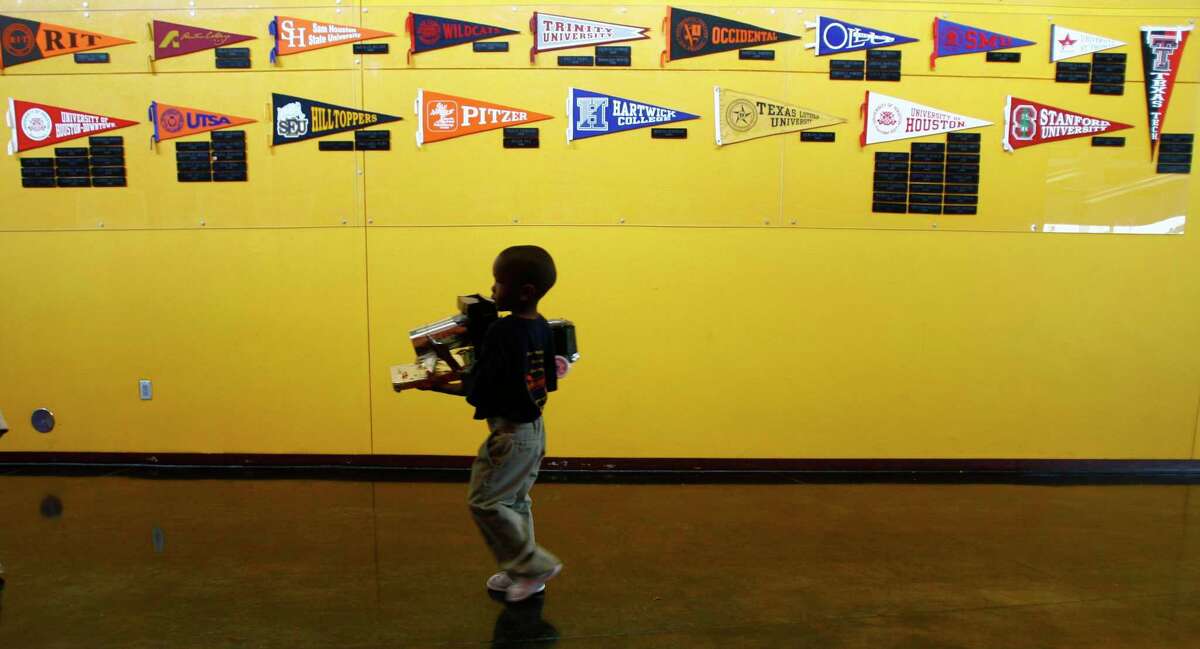 A pre-Kindergarten student at KIPP Academy Elementary School carries a truck made by a class mate to P.E. under the Wall of Fame at KIPP Southeast Academy Middle School in Houston. The wall represents students who graduated 8th-grade from KIPP who are attending colleges and universities across the U.S.