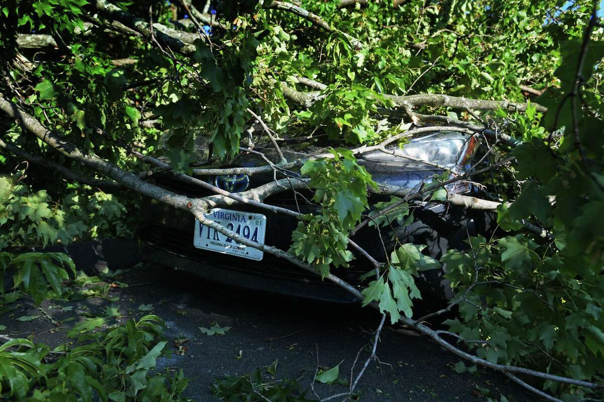 A car is buried under a tree limb near Williams Street in damage wrought by tropical storm Isaias on Wednesday in Norwalk.