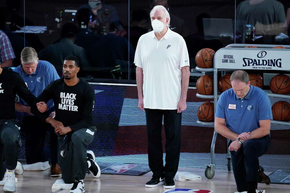 San Antonio Spurs head coach Gregg Popovich stands beside his players as they kneel before an NBA basketball game against the Memphis Grizzlies, Sunday, Aug. 2, 2020, in Lake Buena Vista, Fla. (AP Photo/Ashley Landis, Pool)