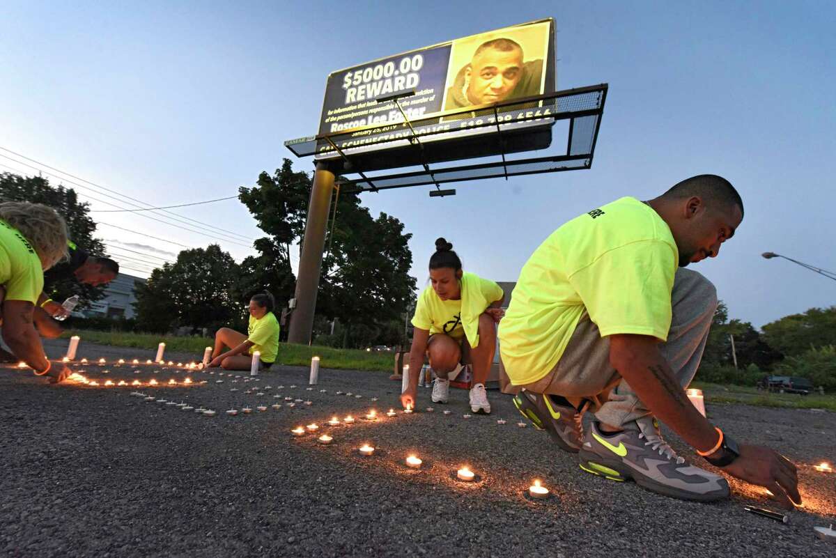 People help light candles during a candlelight vigil at the intersection of State Street and Brandywine Avenue to draw attention to the unsolved 2019 shooting death of Roscoe Foster on Thursday, Aug. 6, 2020 in Schenectady, N.Y. A reward billboard is seen in the background. (Lori Van Buren/Times Union)