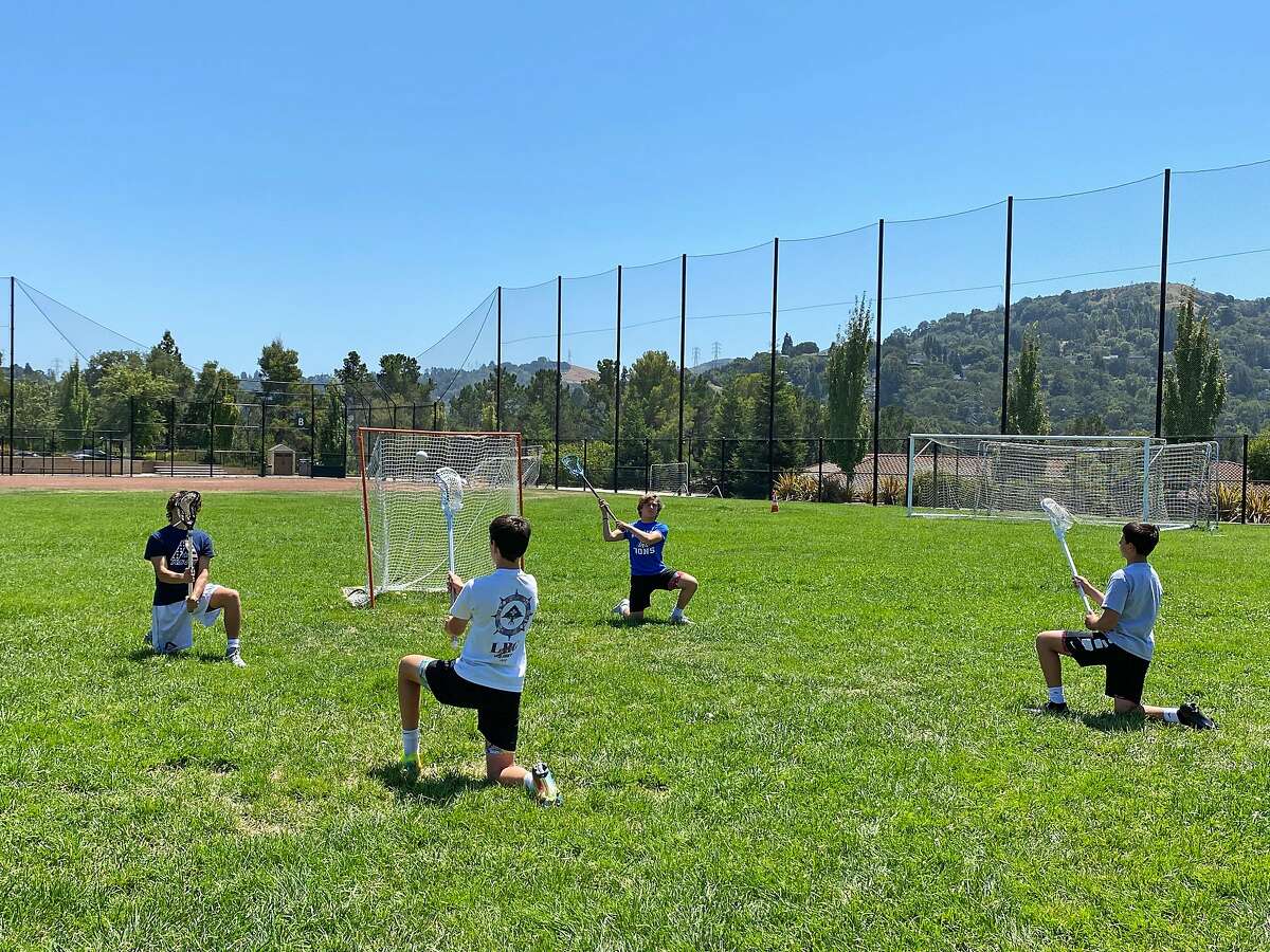Lacrosse players Zach Appel (center right) and Owen Estee (far left) conduct a lacrosse lesson at Pine Grove Park in Orinda, Calif. on Thursday, August 6, 2020. The two teen lacrosse players are raising money to fight hunger during the pandemic by giving lacrosse lessons to other kids while their own high school lacrosse program is suspended because of the pandemic. They call it Lacrosse Against Hunger and they have raised $2000.
