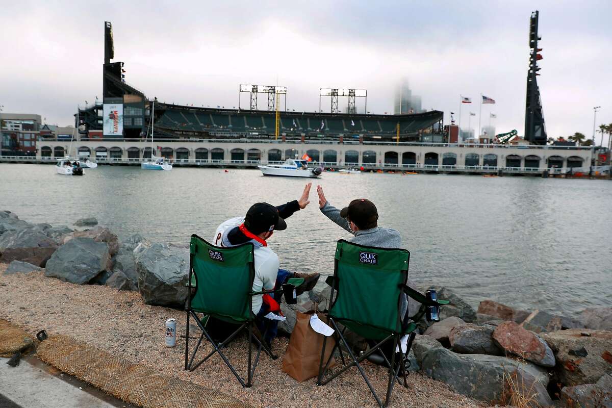 From their seats across McCovey Cove, San Francisco Giants' fans Armando Gonzalez and Dylan Gubrey high five after the Giants score in 1st inning of home opener at Oracle Park in San Francisco, Calif., on Tuesday, July 28, 2020.