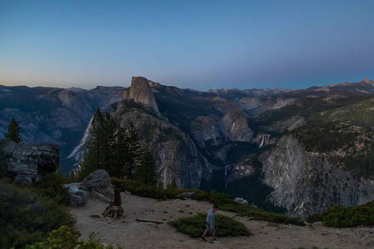 Dusk falls over Half Dome (C L) and Nevada Fall (C R) as a visitor walks at Glacier Point in the Yosemite National Park, California on July 07, 2020. - After closing for 2� months because of the coronavirus pandemic, the wildlife is taking over of areas used by the public. The park is open with limited services and facilities to those with day-use reservations, reservations for in-park lodging or camping, and wilderness or Half Dome permits. (Photo by Apu GOMES / AFP) (Photo by APU GOMES/AFP via Getty Images)