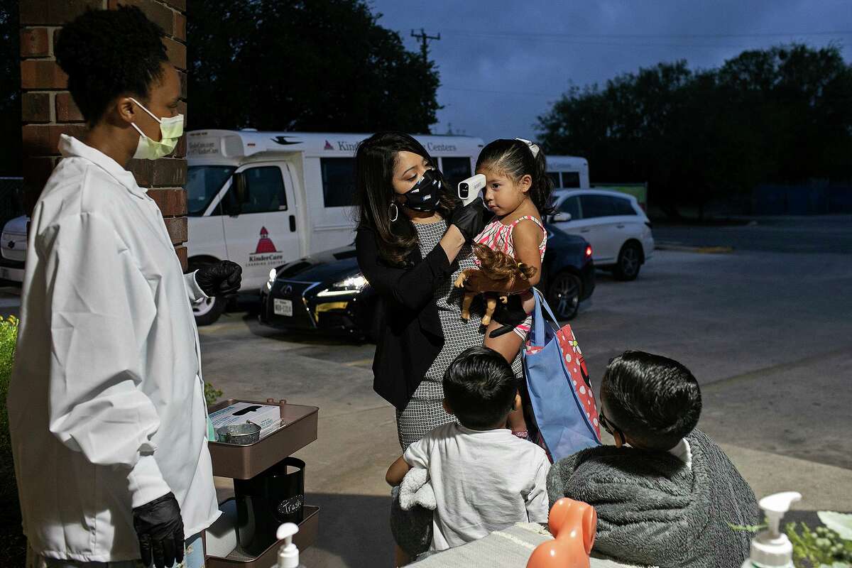 Timber Path KinderCare assistant director Quiana Croom, left, watches as Cecilia Flores takes the temperature of her daughter, Mila, 2, as her sons, Jesiah, 5, and Joel, 6, wait their turn at Timber Path KinderCare.