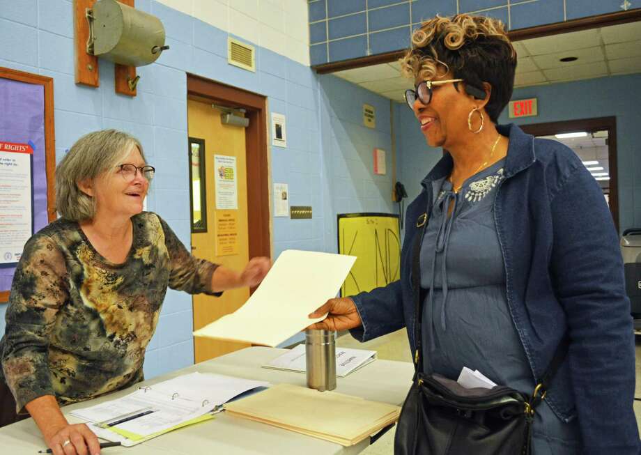 In this archive picture, Middletown resident and election moderator Ann Smith, left, hands a manila folder to a city resident at Macdonough Elementary School during last year’s primary vote. Photo: Hearst Connecticut Media File Photo