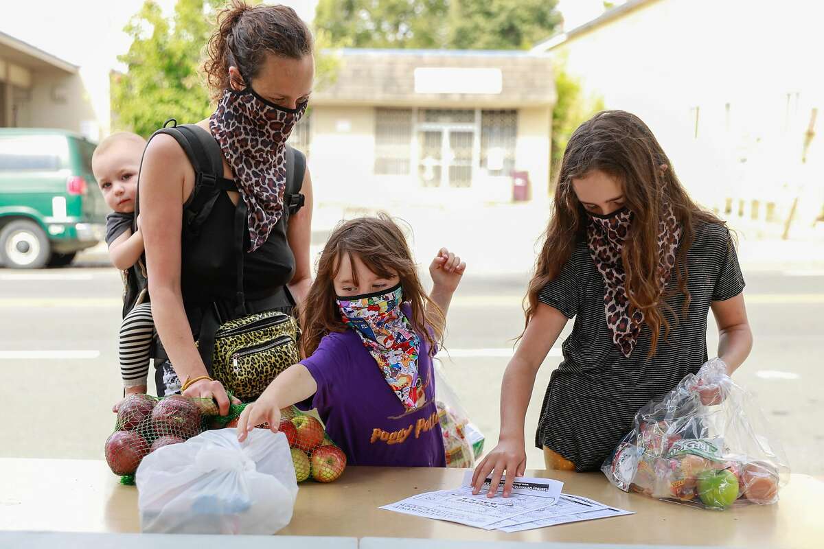 (L-r) Shel Jaeger, 1, mother Eleza Jaeger and her daughters Rhye Jaeger, 6 and Hazel Jaeger, pick up food and supplies at Sankofa Academy on the first day of school on Monday, Aug. 10, 2020 in Oakland, California.