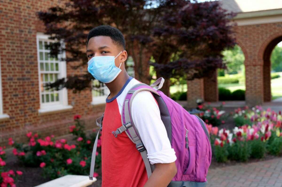 African American teenager wearing backpack and facial mask to protect himself from Coronavirus.