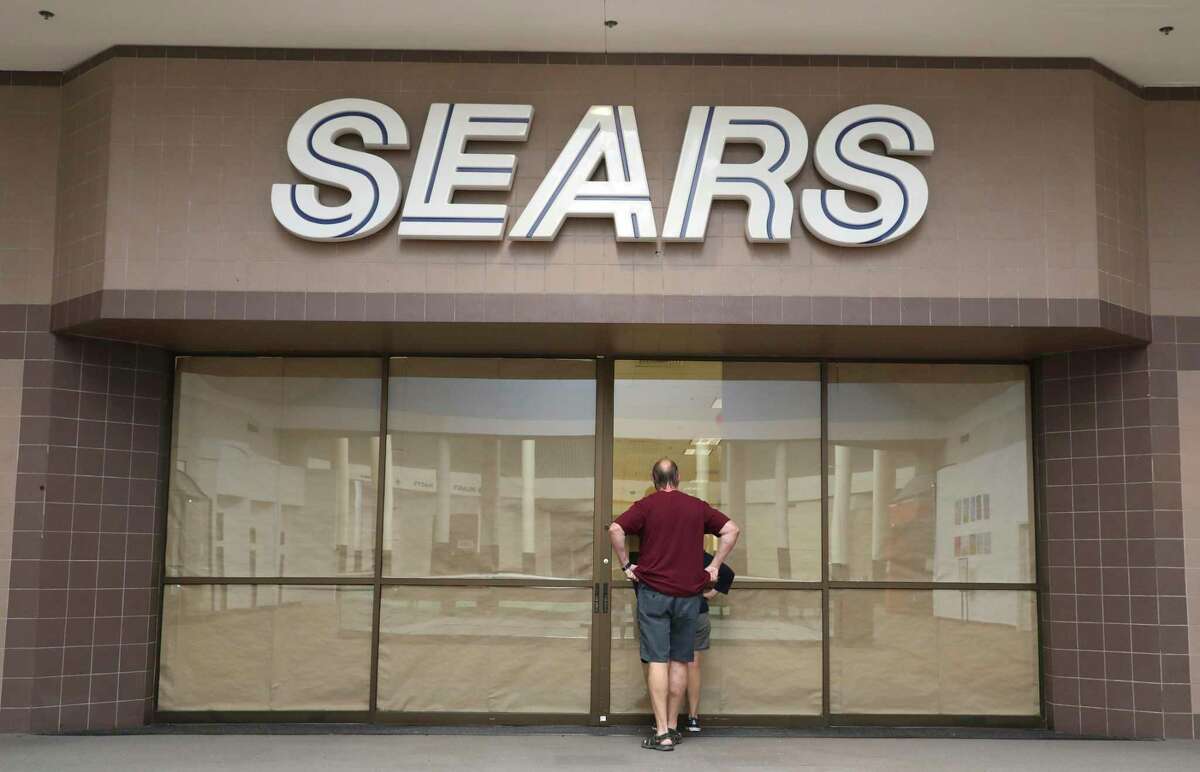 A couple peers through an opening in the papered-over entrance of the Sears store at Rolling Oaks Mall on Tuesday, Aug. 11, 2020.