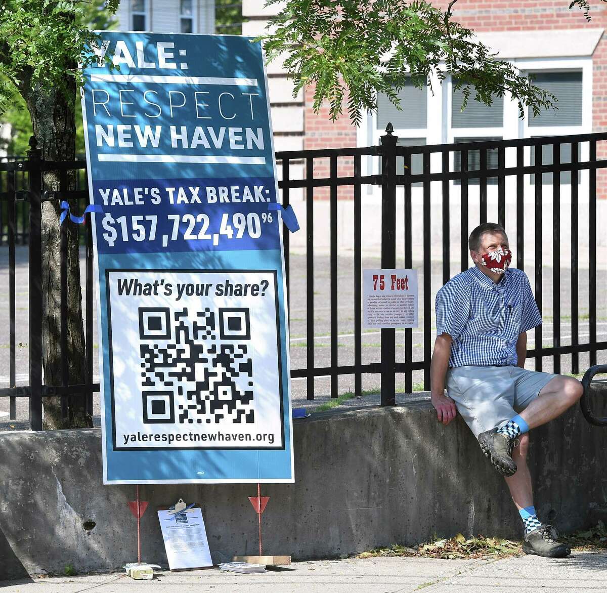 New Haven Alder Adam Marchand sits outside of the Edgewood School polling place in New Haven on Aug. 11, 2020, next to a sign about Yale University’s tax exemption.