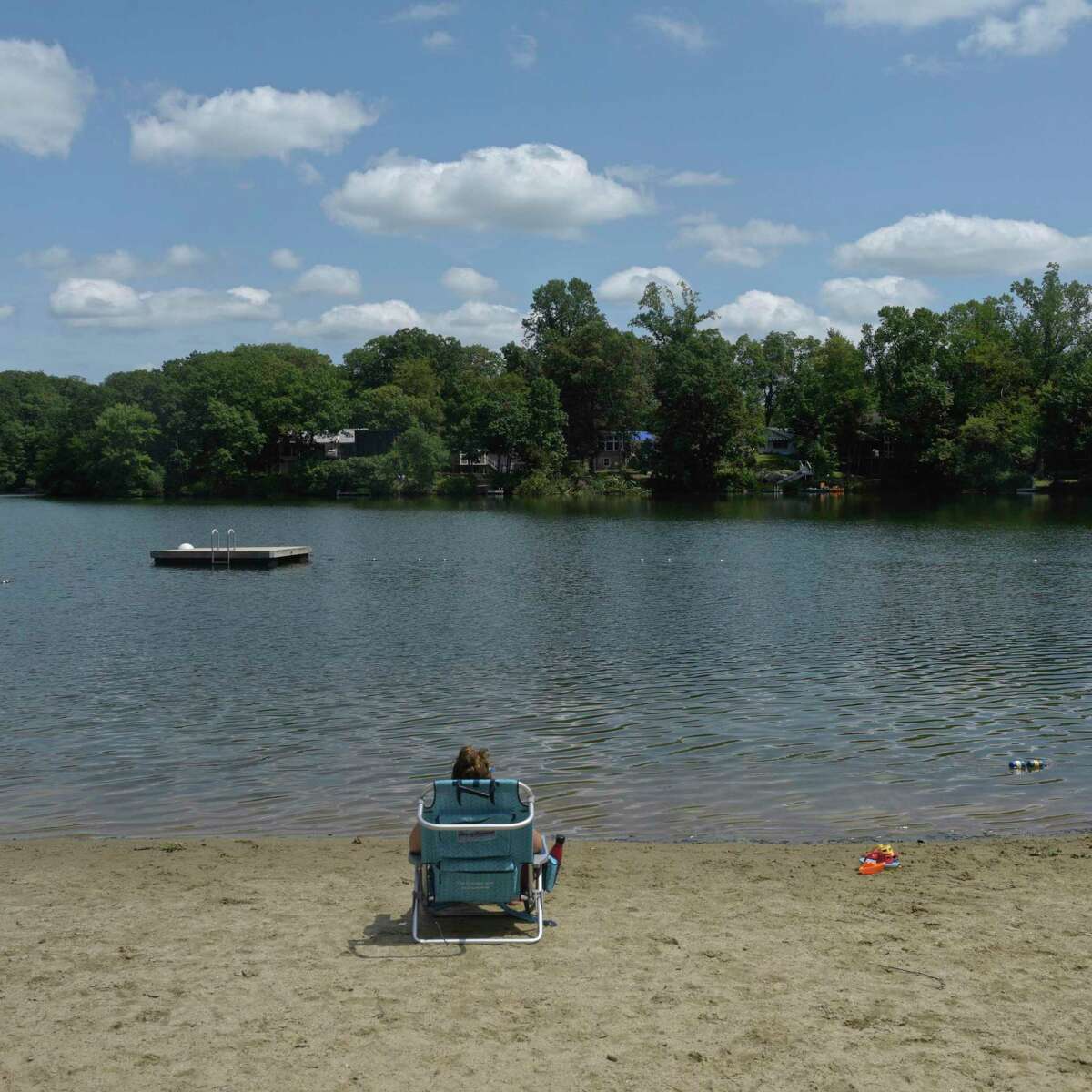 A woman sits on the beach in the Lake Waubeeka community in Danbury, Conn. August 12, 2020.