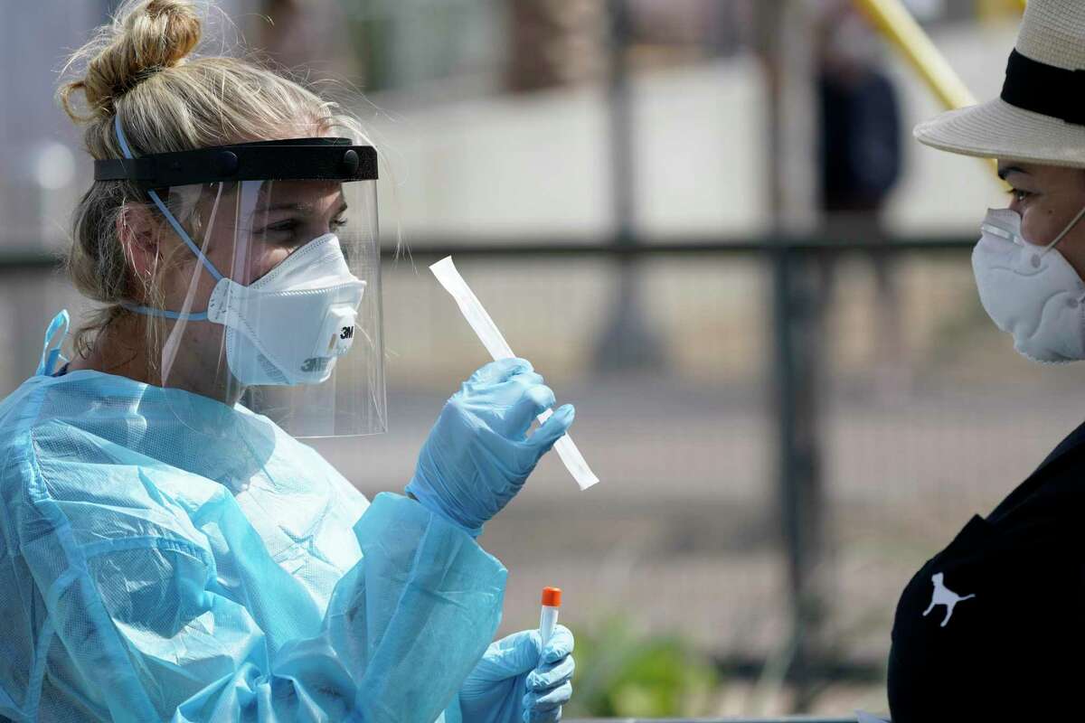 Nurse practitioner Debbi Hinderliter, left, collects a sample from a woman at a coronavirus testing site near the nation's busiest pedestrian border crossing, Thursday, Aug. 13, 2020, in San Diego. San Diego County has started operating a testing site next to the city's largest pedestrian link to Tijuana, Mexico. (AP Photo/Gregory Bull)