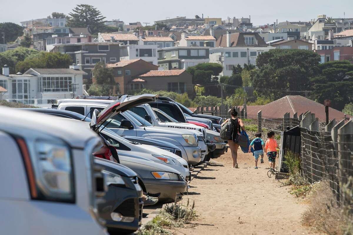 A person and children leave Baker Beach on Thursday, Aug. 13, 2020, in San Francisco, Calif. The parking lot is filled with cars, despite the closed Bowley Street, which leads to the access road to Baker Beach. People are driving past the road closure to reach the parking lot.