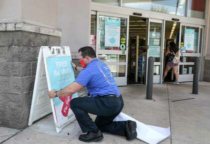 John Kalvaitis, store manager, puts up a sign advertising flu shots Thursday, Aug. 13, 2020, at a Walgreens location in Houston.