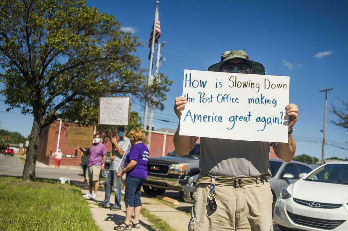 Eric Severson holds a sign as a few dozen people gather in front of the United States Post Office in Midland, Mich., to protest recent changes to the U.S. Postal Service under new Postmaster General Louis DeJoy Tuesday, Aug. 11, 2020 in Midland, Mich.