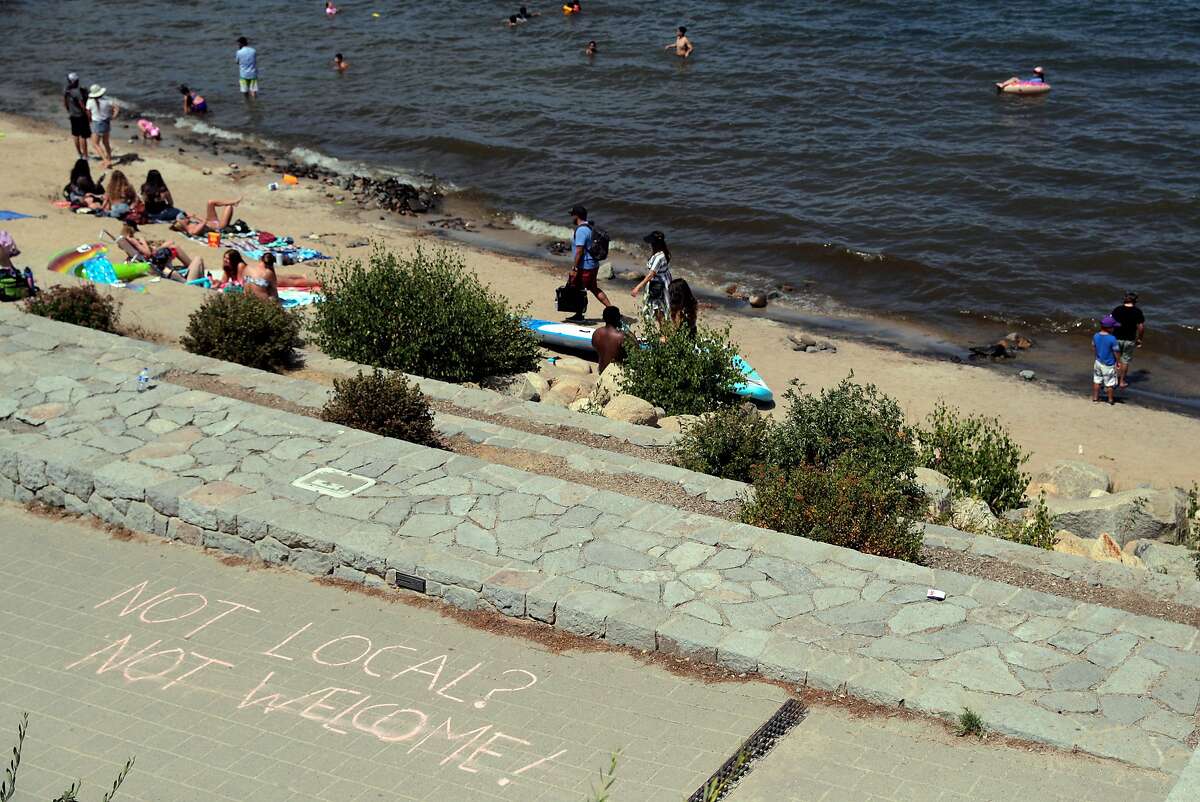 Visitors play on El Dorado Beach above a promenade where someone had written in chalk, "Not Local? Not Welcome!" in South Lake Tahoe, Calif., on Friday, August 14, 2020. There is tension growing in local communities around the lake as out-of-towners are overrunning the Lake Tahoe beaches, littering and they're not wearing face masks or socially distancing, sparking fears of a coronavirus outbreak in Placer County.