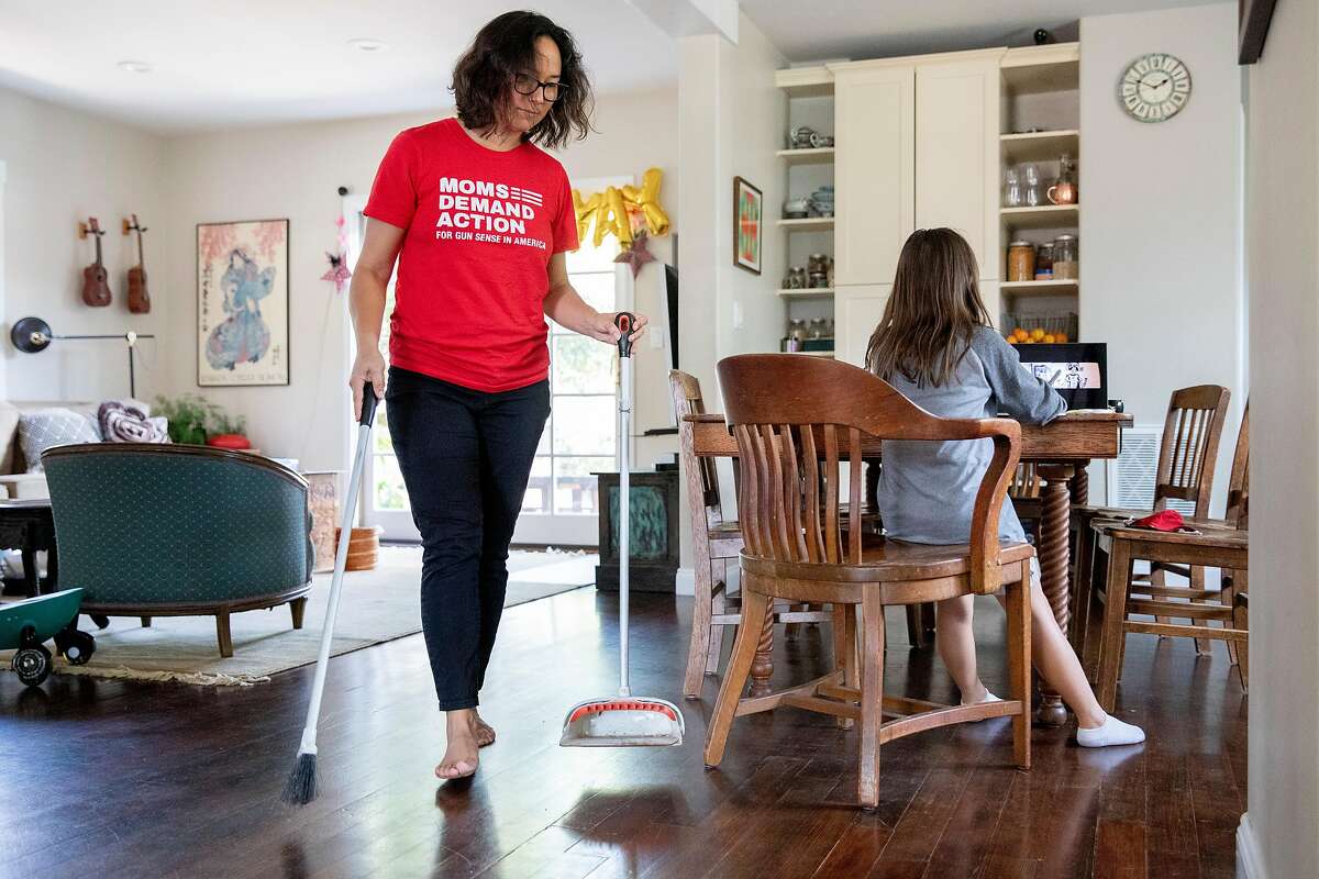 San Mateo City Council  Member Amourence Lee sweeps up the kitchen while her daughter Mia Lin, 8, participates in a video chat art class at their home in San Mateo in August.
