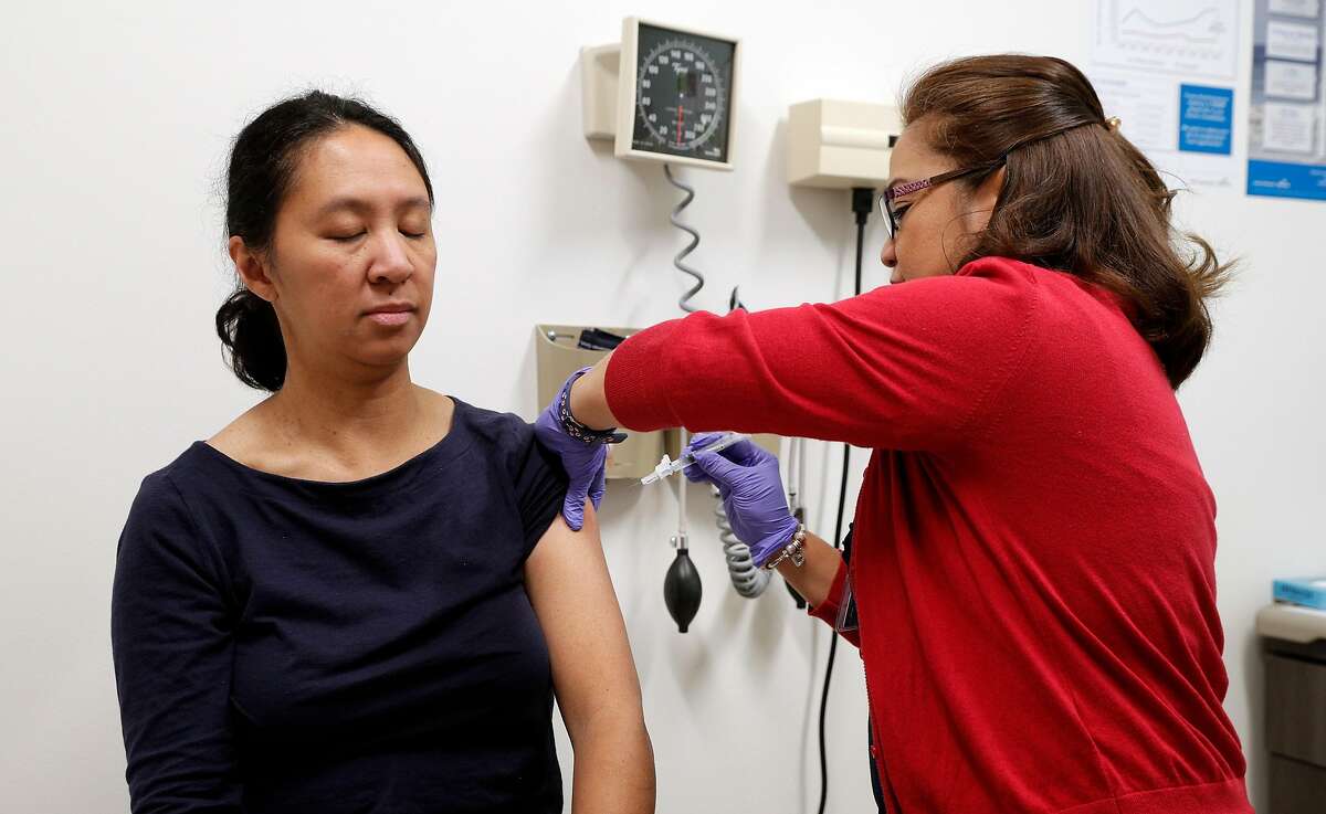 LVN Ilda Villahermosa, right, injects Melanie Valdez with a flu vaccine shot at the Kaiser Permanente Redwood City hospital in Redwood City, Calif., on Thursday, December 28, 2017.