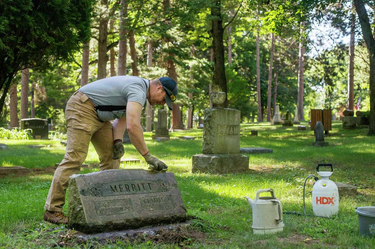 Justin Frost of Midland cleans the headstone of Gilbert and Glatise Merritt as part of his new business, called "Past Preservation," Wednesday, Aug. 12 at Midland Municipal Cemetery. (Katy Kildee/kkildee@mdn.net)