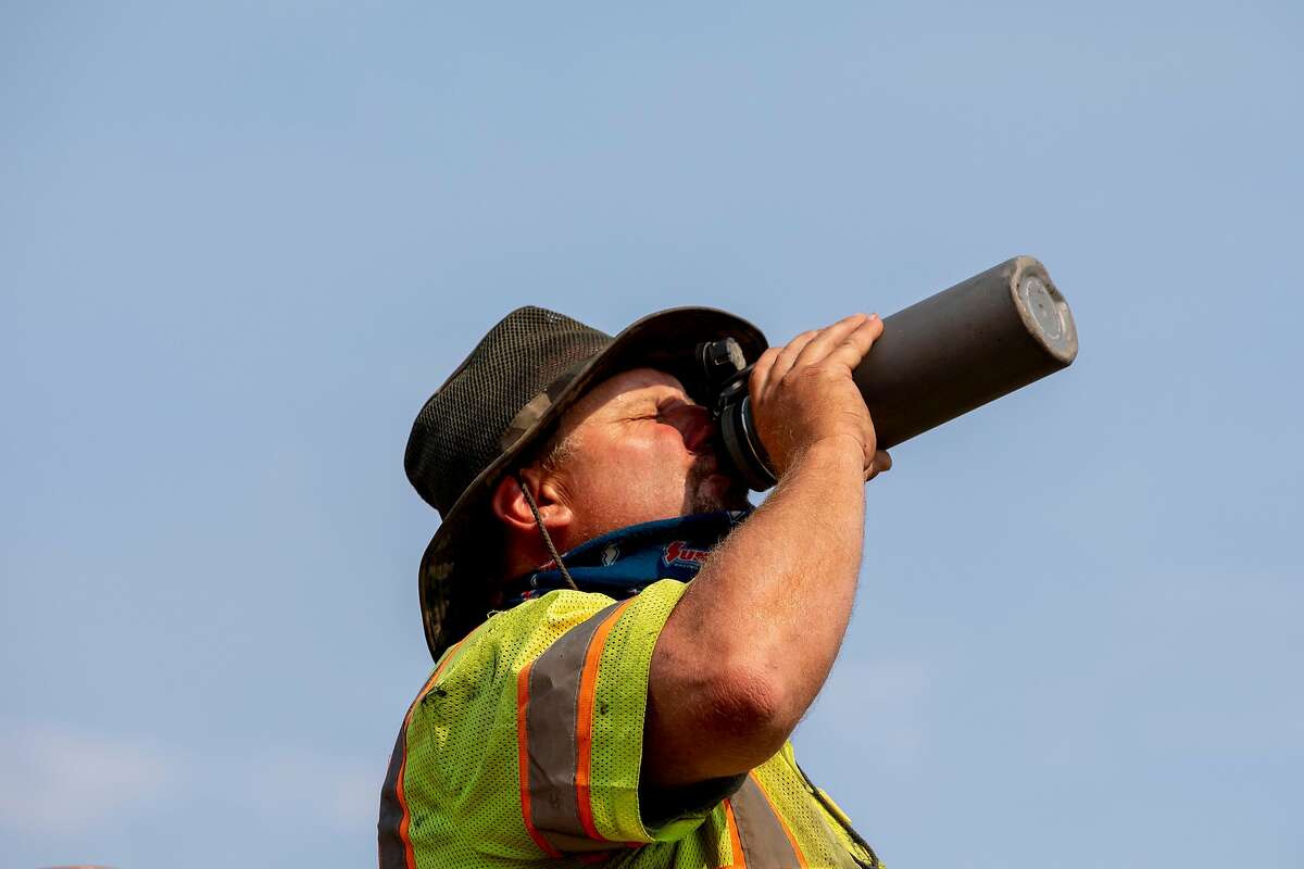 A Contra Costa Public Works maintenance crewmember drinks from a water bottle while completing a chip seal operation on Christie Road in Martinez, Calif. Tuesday, August 18, 2020. City employees and road crews have been working in extreme temperatures during the Bay Area heat wave and stay cool by wearing shaded hats and drinking water consistently.