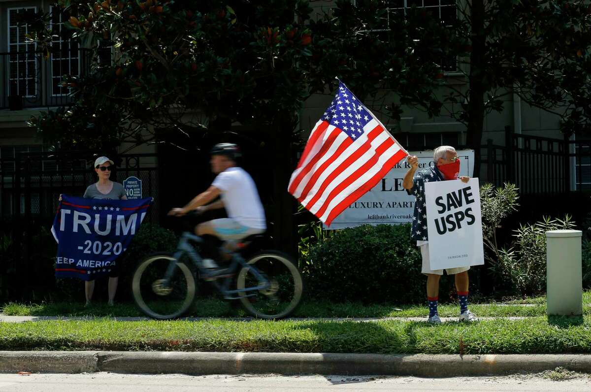 Rachal Smith, left, shows her support for President Donald Trump, as Ira Dember, right, waves an American flag and holds up a sign that reads "Save USPS," during a protest outside Senator John Cornyn's office Tuesday, Aug. 18, 2020, in Houston.