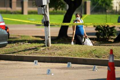 A woman wearing a mask walks past a homicide scene, Friday, March 27, 2020, at a strip mall center in west Houston.