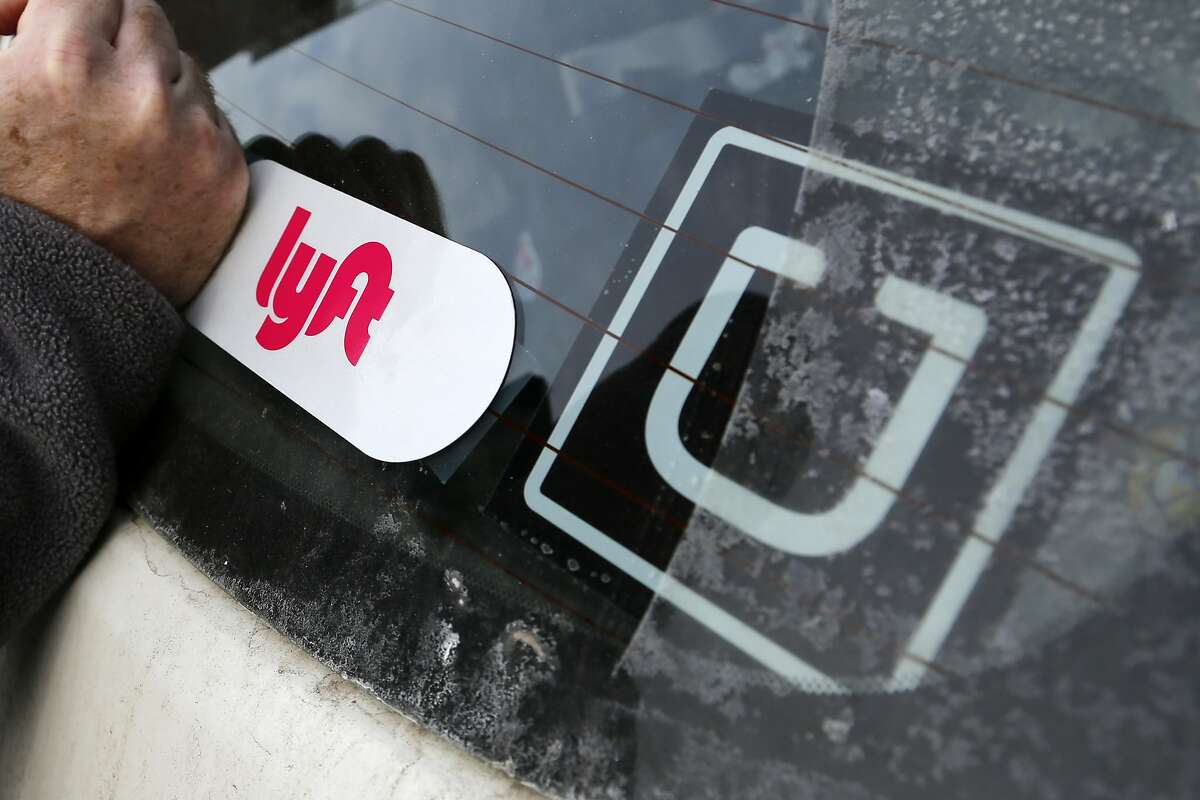 FILE- In this Jan. 31, 2018, file photo, a Lyft logo is installed on a Lyft driver's car next to an Uber sticker in Pittsburgh. Ride-hailing giants Uber and Lyft on Thursday, Aug. 20, 2020, are saying they will shut down their California operations if a new law goes into effect overnight which would force both companies to classify their drivers as employees. (AP Photo/Gene J. Puskar, File)