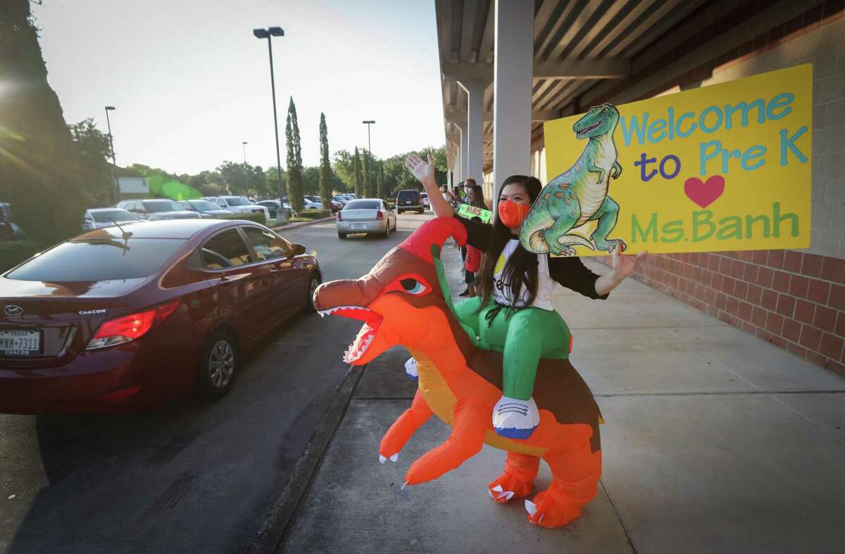 Ms. Diana Banh waves and greets students in a dinosaur costume during a car parade for pre-K pupils and kindergarteners at Stafford MSD's Early Childhood Center Wednesday, Aug. 19, 2020, in Stafford. Students met their teachers from social distance of their cars.