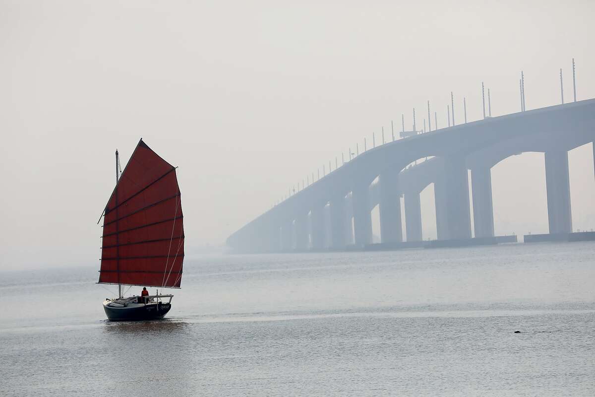 A sailboat named Quest passes the Bay Bridge as a smoky haze from multiple wildfires in the Bay Area continues to fill the morning sky from Treasure Island, Calif., on Friday, August 21, 2020.