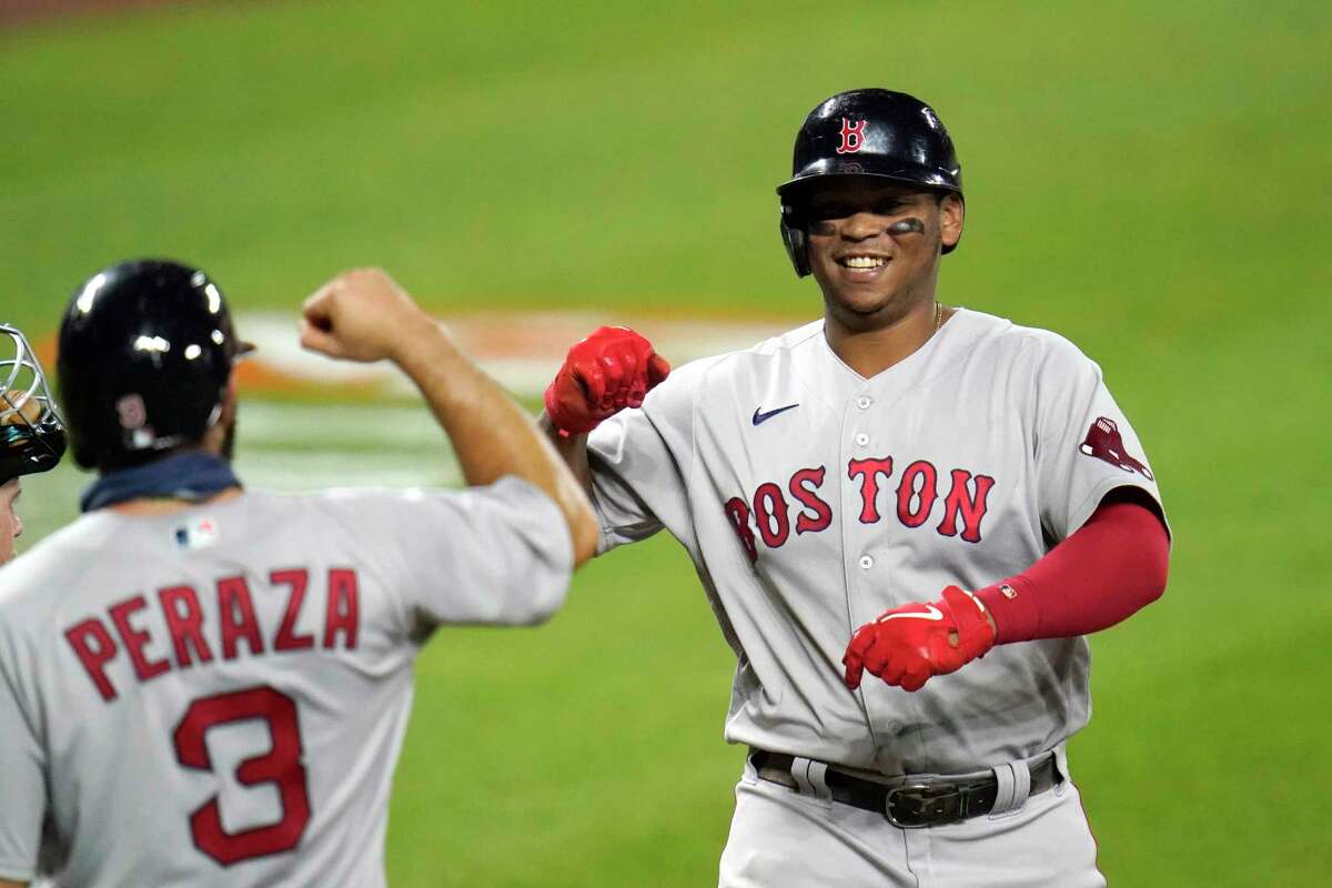 Boston Red Sox's Rafael Devers, right, is greeted near home plate by Jose Peraza (3) after Devers hit a three-run home run off Baltimore Orioles relief pitcher Jorge Lopez during the fifth inning of a baseball game, Friday, Aug. 21, 2020, in Baltimore. Red Sox's Kevin Pillar, not visible, and Peraza scored on the home run. (AP Photo/Julio Cortez)