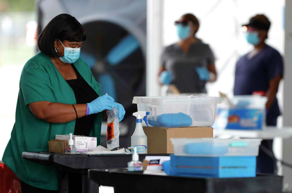 A woman gathers testing supplies for a patient to use a self-administered coronavirus test at Pridgeon Stadium, Friday, July 31, 2020, in Cypress.