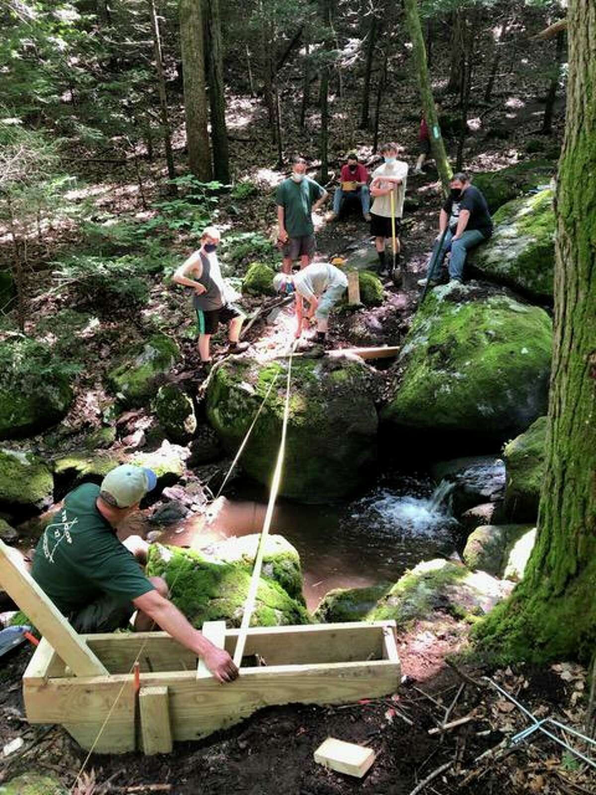 Korey Barber, a Boy Scout with the Housatonic Troop 27 Life Scout and a rising senior at Shelton High School, is organizing construction of a bridge crossing Round Hill Brook on the Paugussett trail. Above, Barber and other volunteers work on creating the bridge.