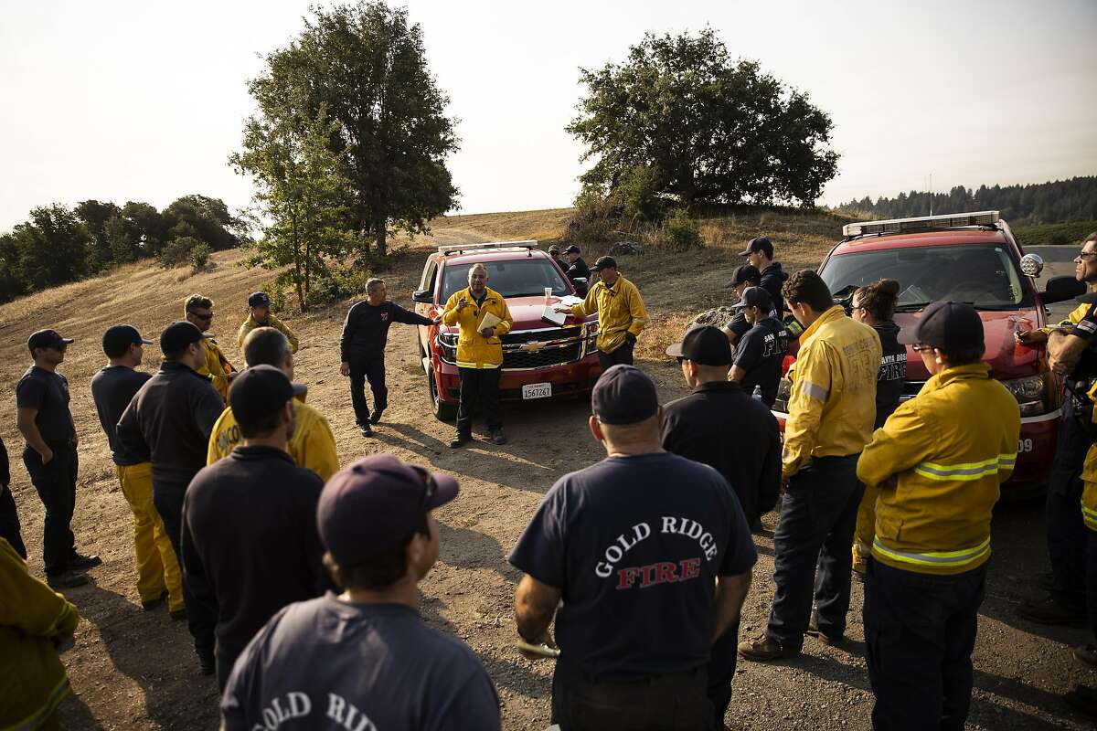 Abe Roman, a deputy fire chief with the Berkeley Fire Department, center, briefs a group of firefighters during the Walbridge fire, part of the burgeoning LNU Lightning Complex Fire that has scorched 314,207 acres and destroyed 506 structures across five counties in Healdsburg, Calif. on Saturday, Aug. 22, 2020. The LNU Lightning Complex Fire is currently 15% contained.