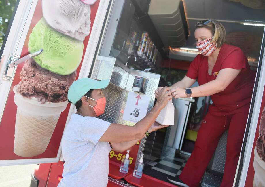 Stamford Senior Center Executive Director Christina Crain, left, takes ice cream from Ice Cream Emergency Shireen D'Andrea at the ice cream drive-thru for members of the Stamford Senior Center at the Jewish Community Center in Stamford, Conn. Thursday, Aug. 20, 2020. About 150 seniors picked up ice cream from the Ice Cream Emergency truck Thursday afternoon. The Senior Center will host a taco truck drive-thru next month. Photo: Tyler Sizemore / Hearst Connecticut Media / Greenwich Time