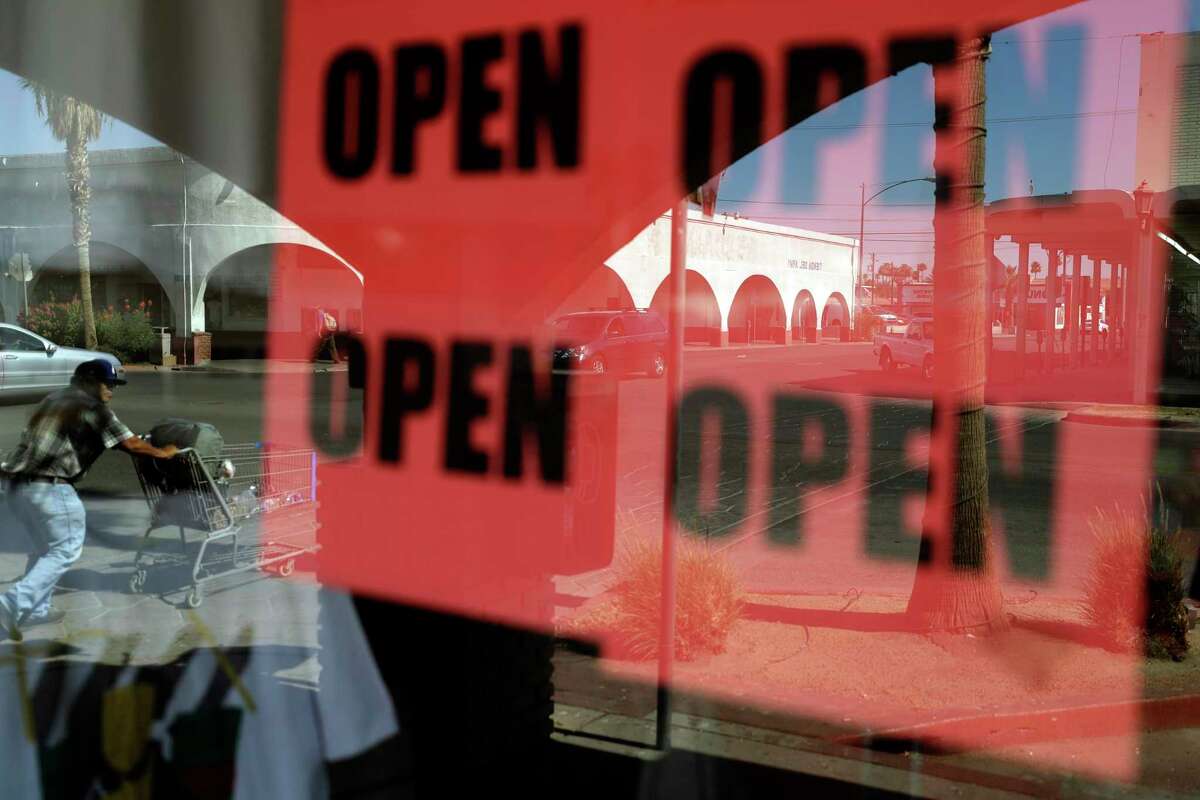 FILE - In this June 30, 2020, photo, a man passes a clothing shop with open signs in the window in Calexico, Calif. Records obtained by The Associated Press show governors working closely with business interests as they weighed when and how to reopen their economies during the coronavirus pandemic. (AP Photo/Gregory Bull, File)