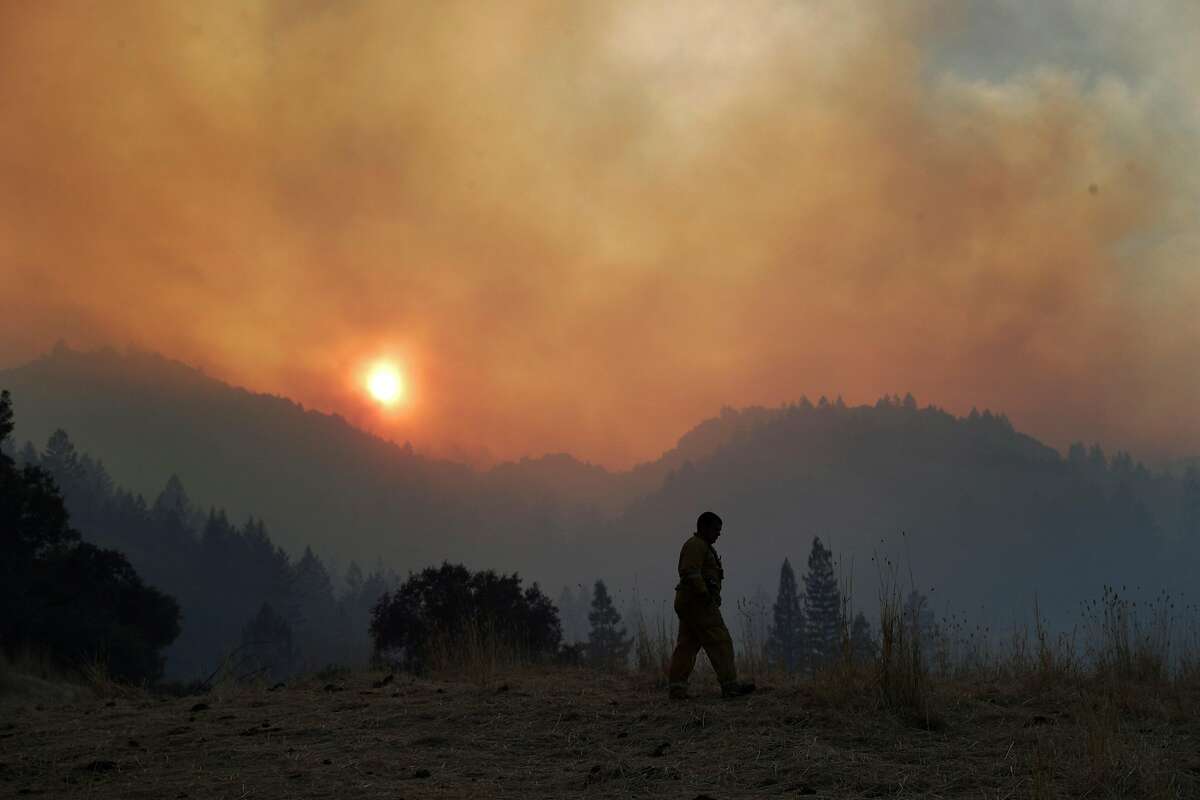 A Santa Rosa firefighter walks along a field off Wine Creek Road while conducting structure protection for the Walbridge Fire west of Healdsburg, Calif., on Friday, August 21, 2020.