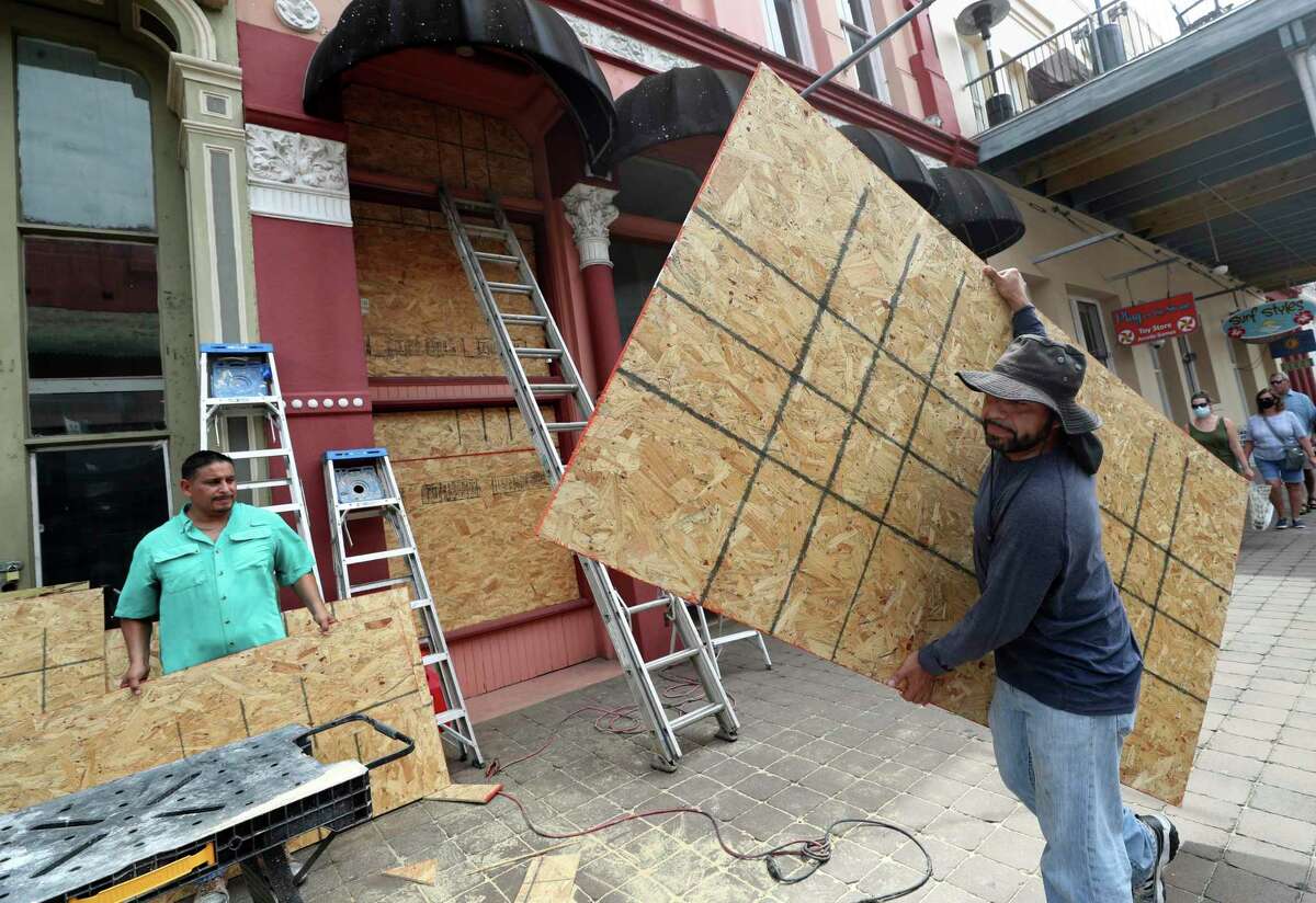 Cesar Reyes, right, carries a sheet of plywood to cut to size as he and Robert Aparicio, left, and Manuel Sepulveda, not pictured, install window coverings at Strand Brass and Christmas on the Strand, 2115 Strand St., in Galveston on Monday, Aug. 24, 2020. Ginger Herter, who manages the shop, was erring on the side of caution boarding up the storefront as she waits to see what path Tropical Storm Laura will take as it heads toward the Texas and Louisiana coasts. "I'd rather do this and have to take them down rather than scramble to get them up later in the week," she said. ( Jennifer Reynolds/The Galveston County Daily News via AP)
